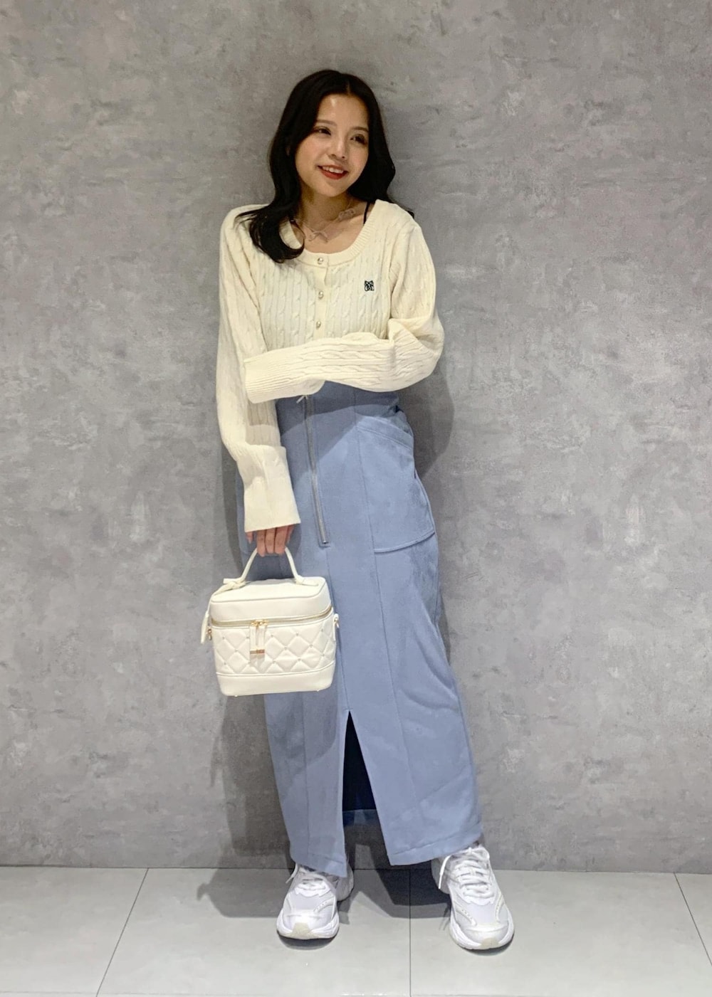 ホワイト系のハンドバッグ、ホワイト系のカーディガン/ボレロ、ブルー系のスカートを着用したレディースの冬コーディネートの2枚目の写真