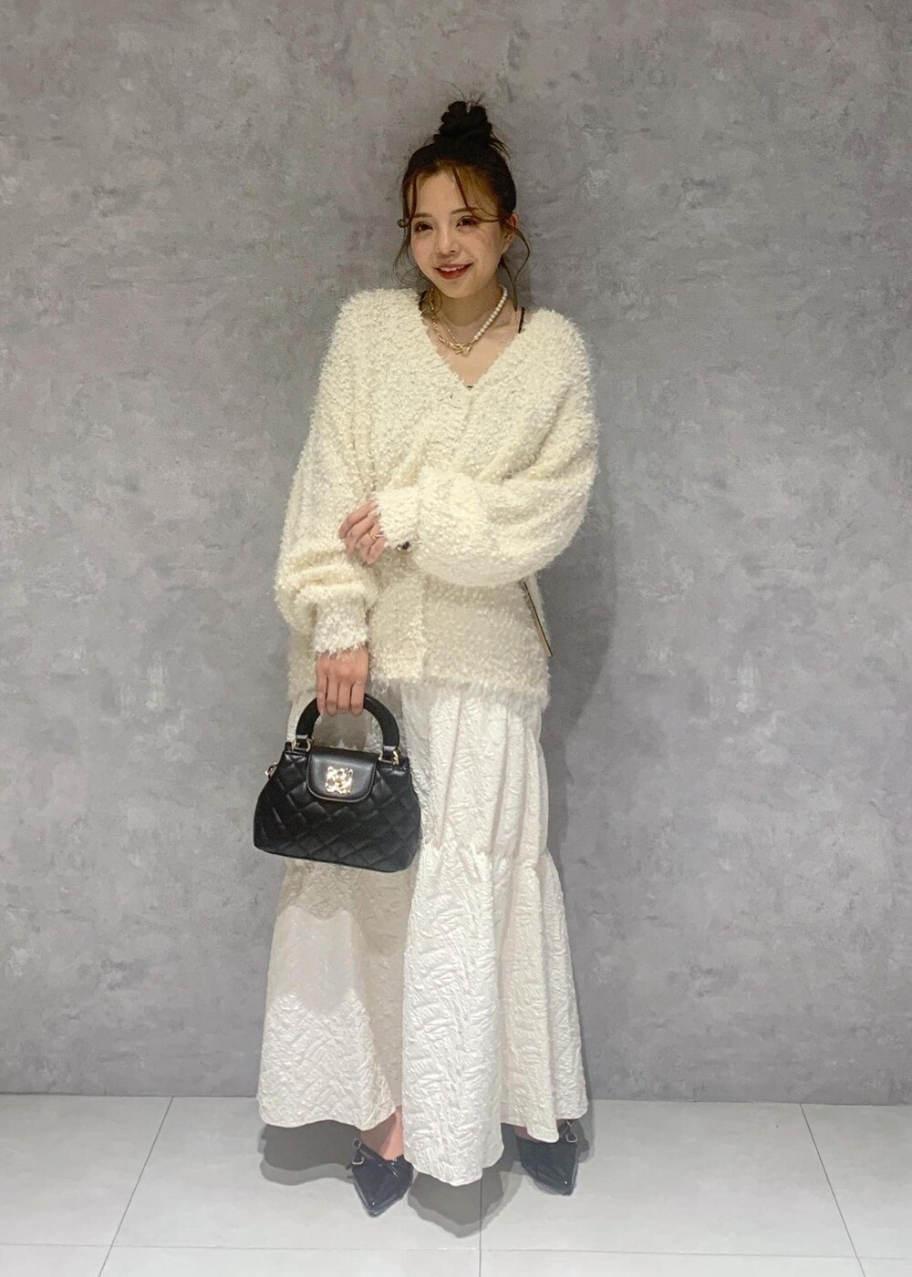 ホワイト系のカーディガン/ボレロ、ブラック系のパンプス、ホワイト系のスカートを着用したレディースの冬コーディネートの2枚目の写真