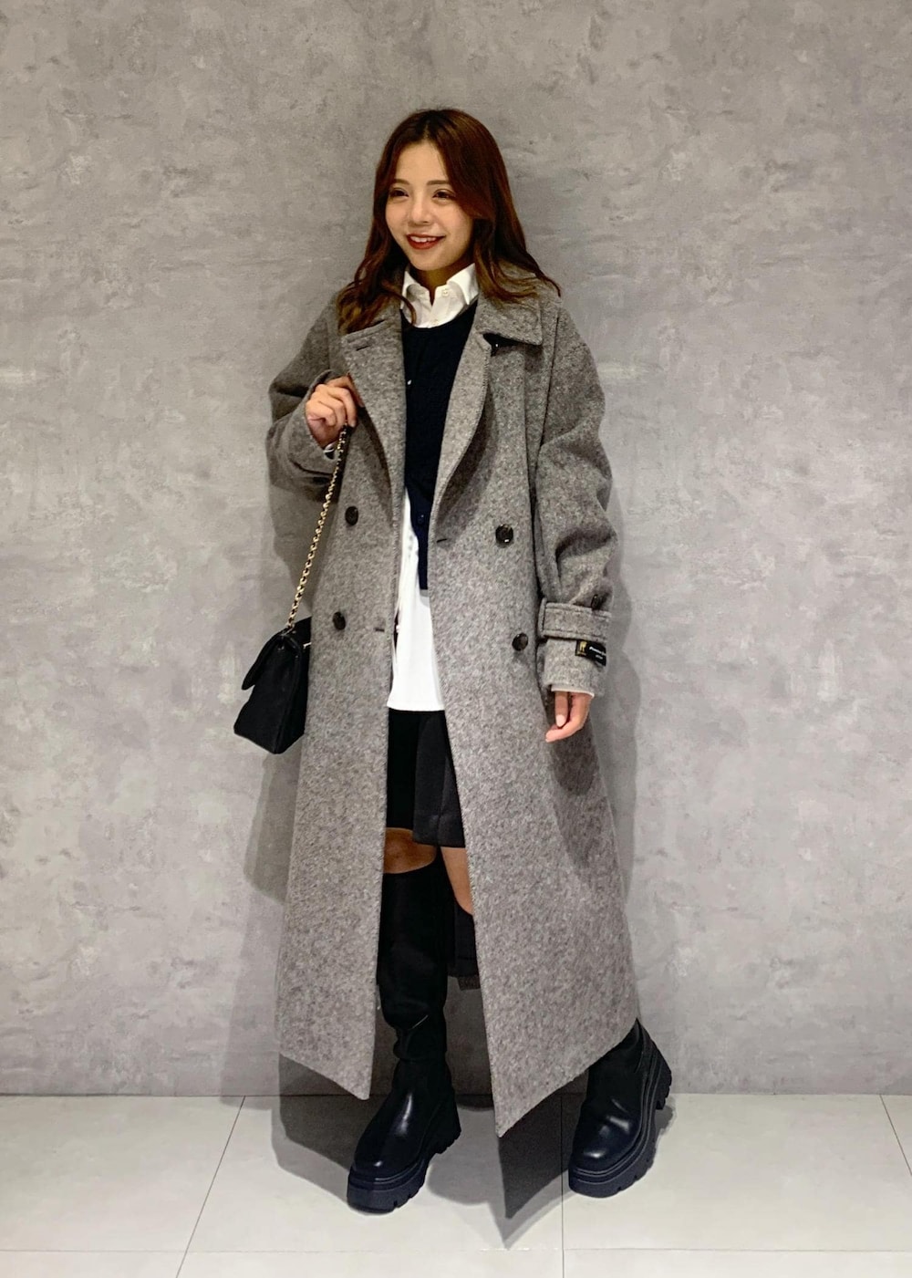 ブラック系のショルダーバッグ、ブラック系のブーツ、グレー系のステンカラーコートを着用したレディースの秋コーディネートの2枚目の写真