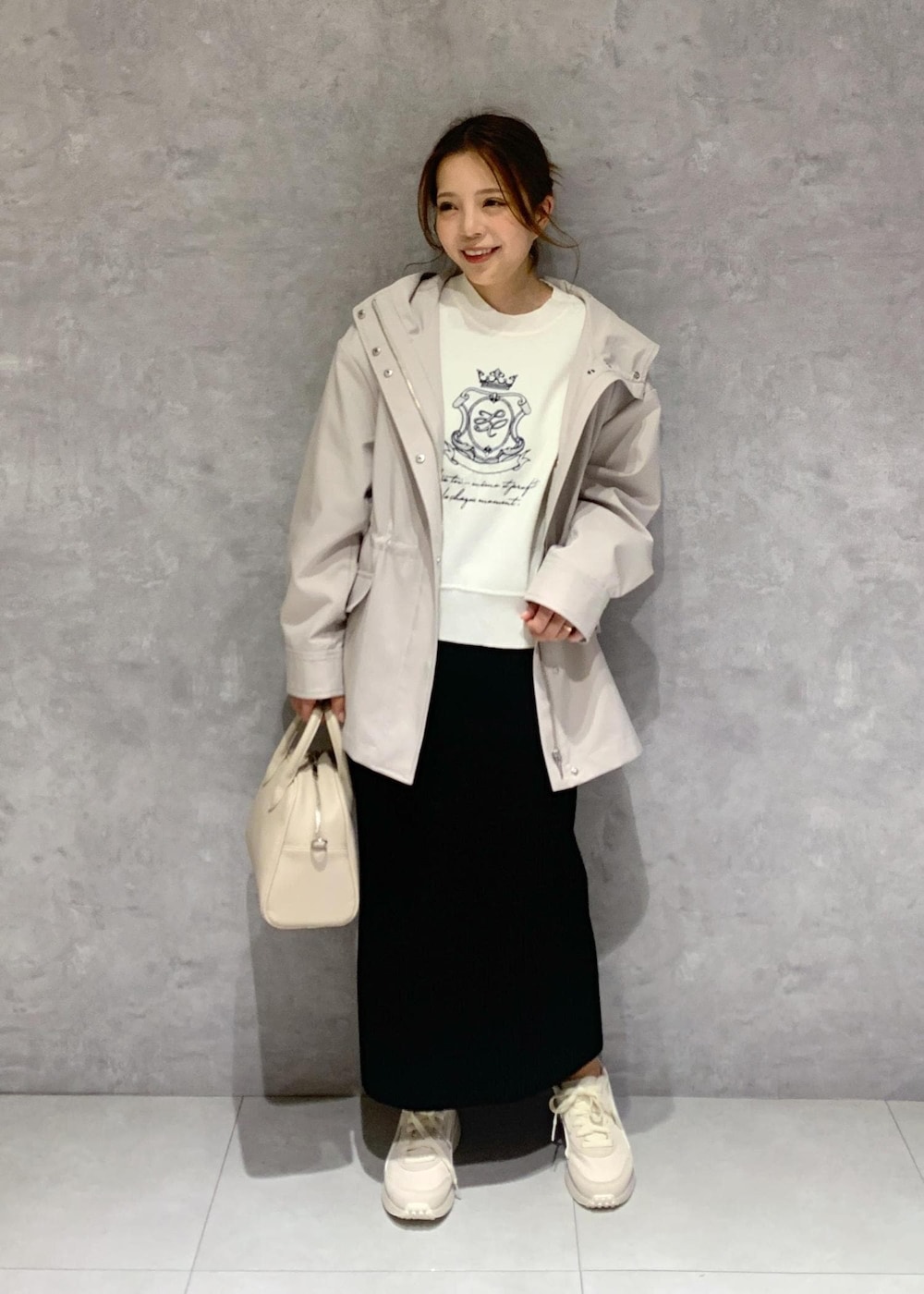 ブラック系のスカート、ベージュ系のボストンバッグ、グレー系のマウンテンパーカーを着用したレディースの春コーディネートの2枚目の写真