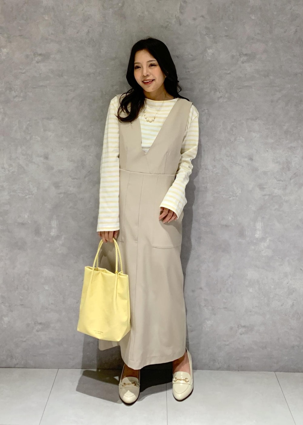 イエロー系のトートバッグ、ベージュ系のジャンパースカート、ベージュ系のTシャツ/カットソーを着用したレディースの冬コーディネートの2枚目の写真