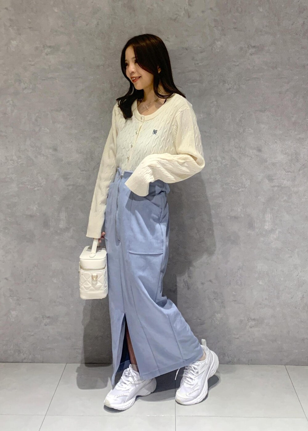 ホワイト系のハンドバッグ、ホワイト系のカーディガン/ボレロ、ブルー系のスカートを着用したレディースの冬コーディネートの3枚目の写真