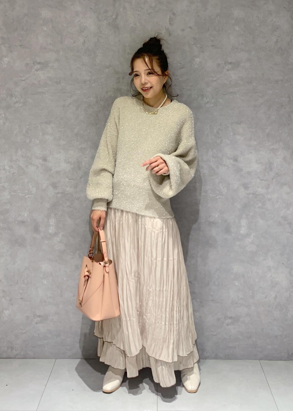 ピンク系のショルダーバッグ、ホワイト系のブーツ、ベージュ系のスカートを着用したレディースの冬コーディネートの2枚目の写真