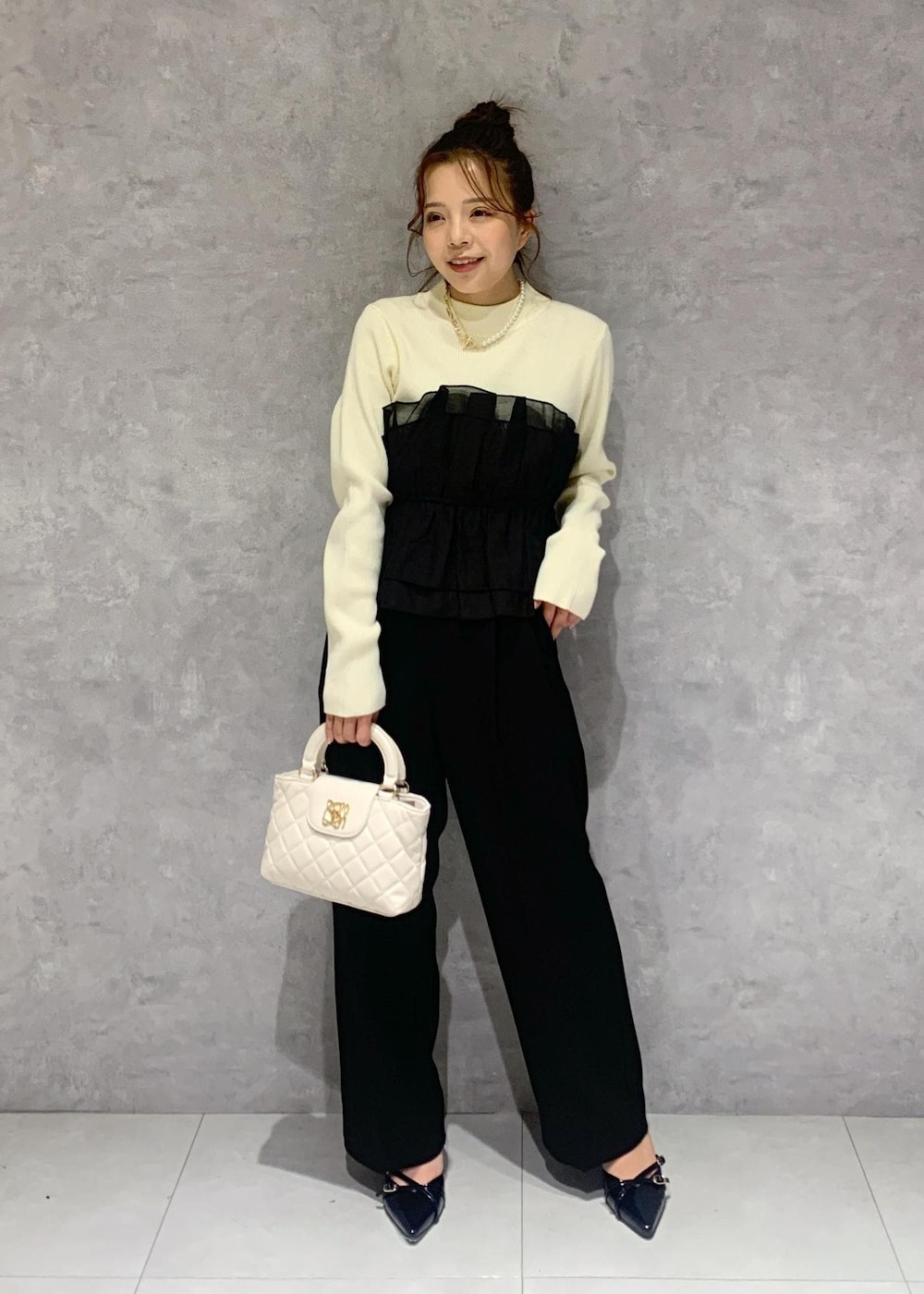 ブラック系のパンプス、ホワイト系のニット/セーター、ブラック系のスラックスを着用したレディースの冬コーディネートの2枚目の写真