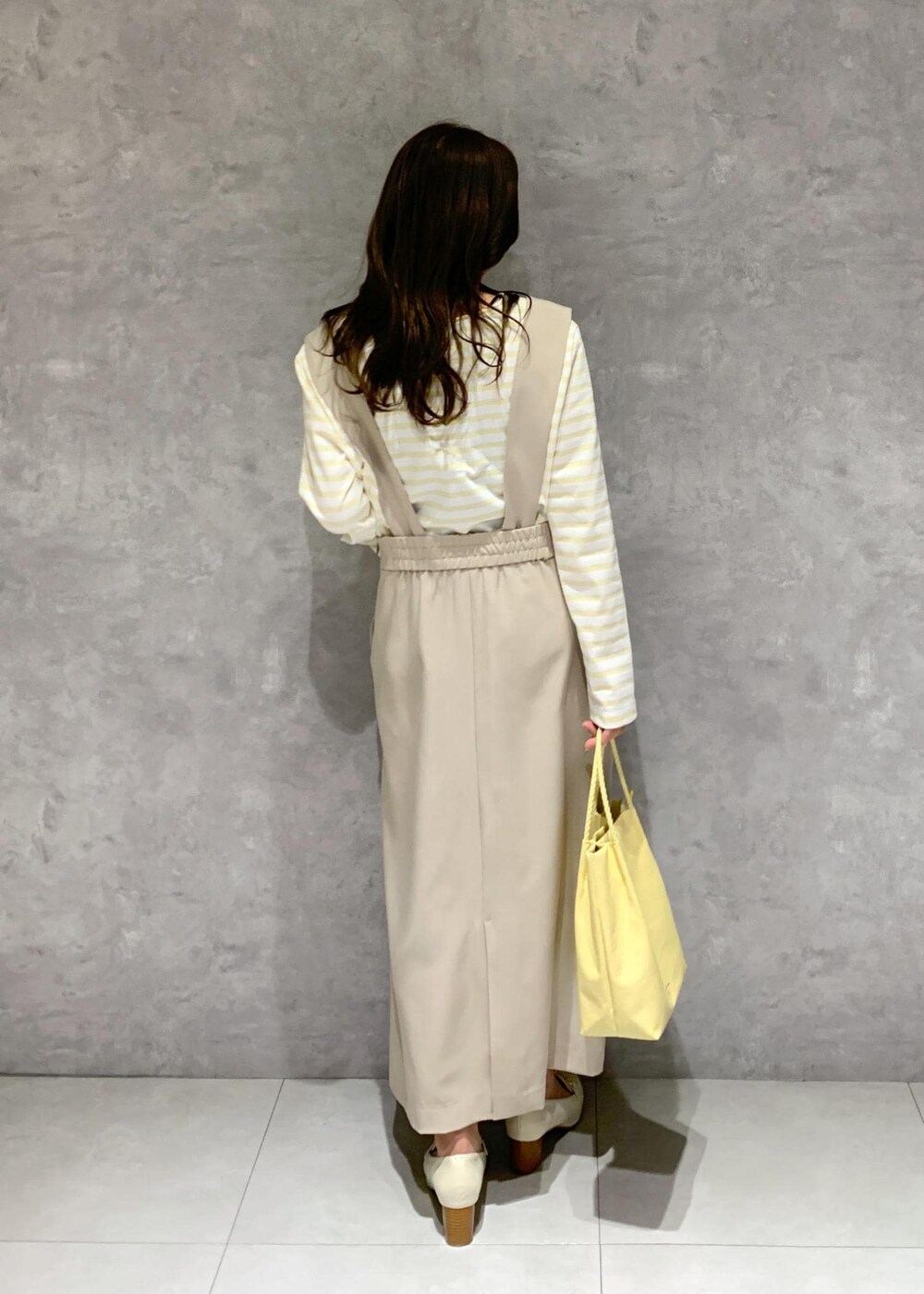 イエロー系のトートバッグ、ベージュ系のジャンパースカート、ベージュ系のTシャツ/カットソーを着用したレディースの冬コーディネートの5枚目の写真