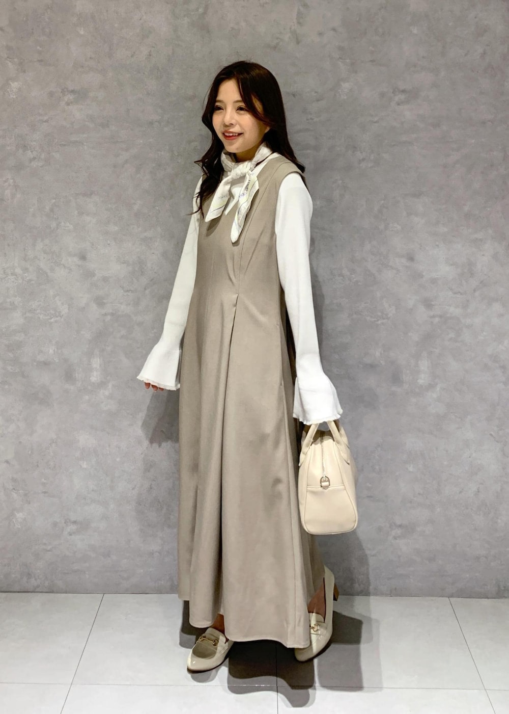 イエロー系のジャンパースカート、ホワイト系のニット/セーター、ホワイト系のローファーを着用したレディースの冬コーディネートの3枚目の写真