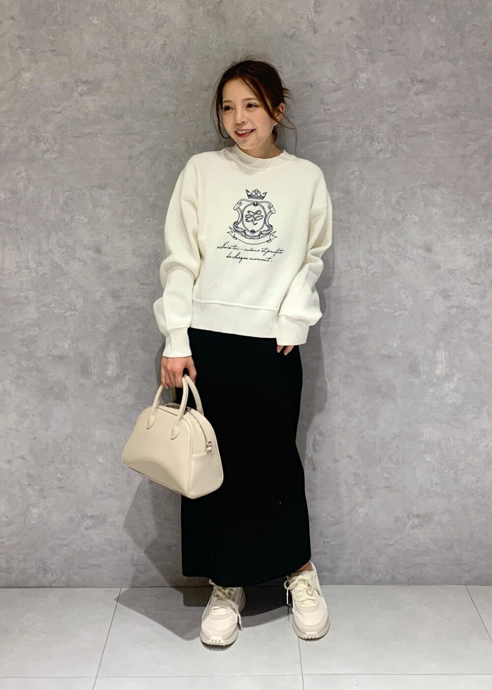 ブラック系のスカート、ベージュ系のボストンバッグ、ホワイト系のニット/セーターを着用したレディースの春コーディネートの2枚目の写真