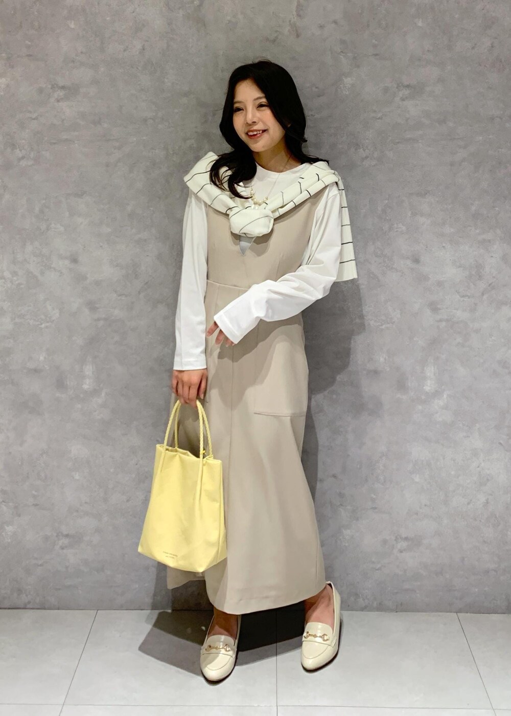 ホワイト系のTシャツ/カットソー、イエロー系のトートバッグ、ベージュ系のジャンパースカートを着用したレディースの冬コーディネートの2枚目の写真