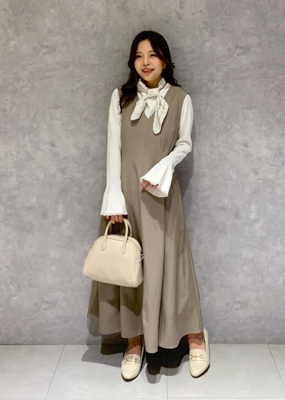 イエロー系のジャンパースカート、ホワイト系のニット/セーター、ホワイト系のローファーを着用したレディースの冬コーディネートの2枚目の写真