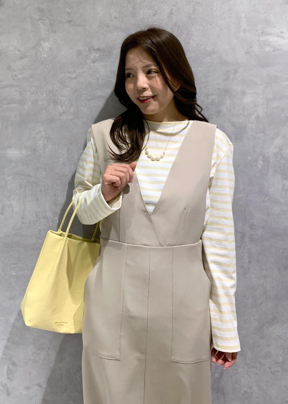 イエロー系のトートバッグ、ベージュ系のジャンパースカート、ベージュ系のTシャツ/カットソーを着用したレディースの冬コーディネートの6枚目の写真