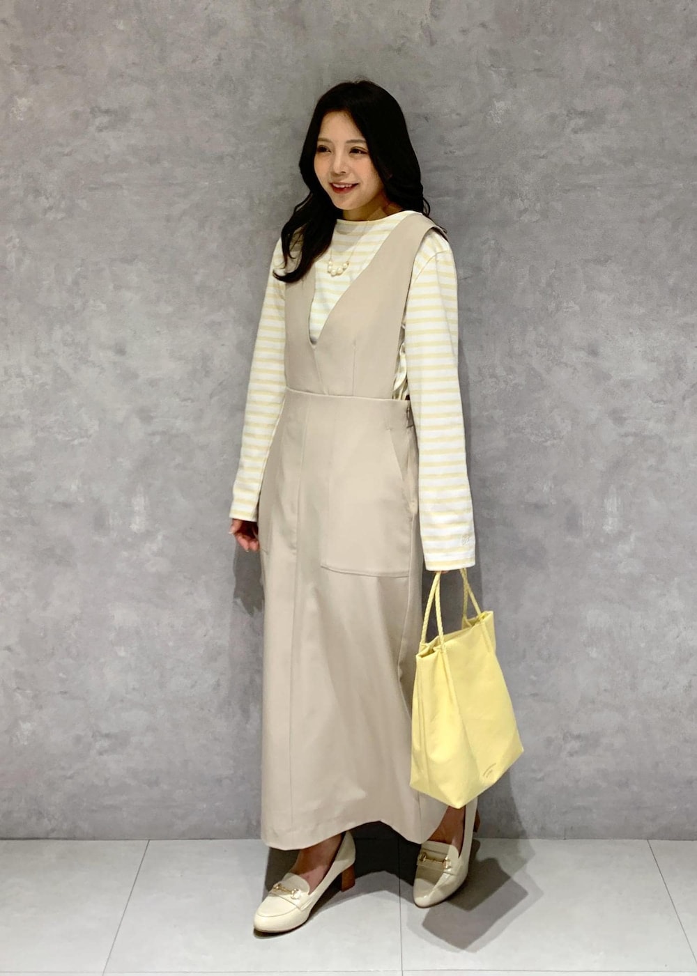 イエロー系のトートバッグ、ベージュ系のジャンパースカート、ベージュ系のTシャツ/カットソーを着用したレディースの冬コーディネートの3枚目の写真