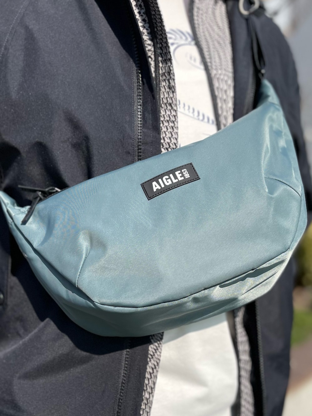 ブラック系のマウンテンパーカー、ブルー系のチノパンツ、グリーン系のショルダーバッグを着用したメンズの冬コーディネートの3枚目の写真