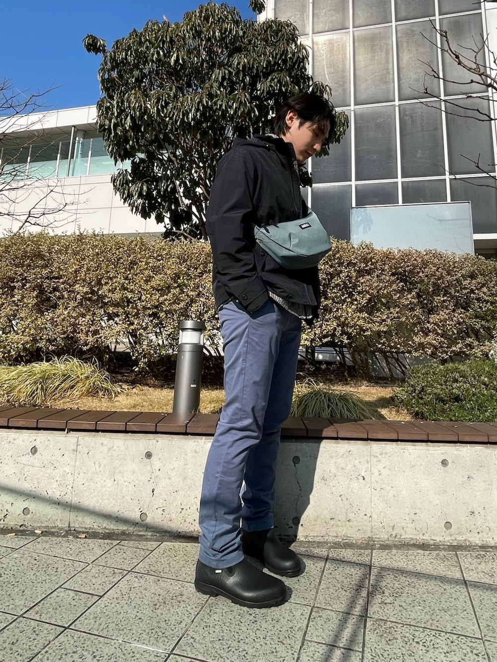 ブラック系のマウンテンパーカー、ブルー系のチノパンツ、グリーン系のショルダーバッグを着用したメンズの冬コーディネートの2枚目の写真