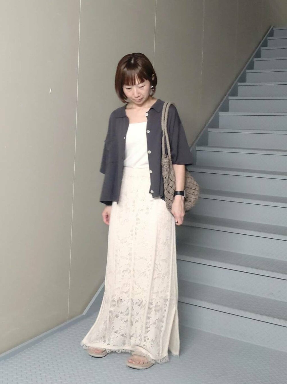 グレー系のトートバッグ、グレー系のニット/セーター、ホワイト系のスカートを着用したレディースの夏コーディネートの3枚目の写真