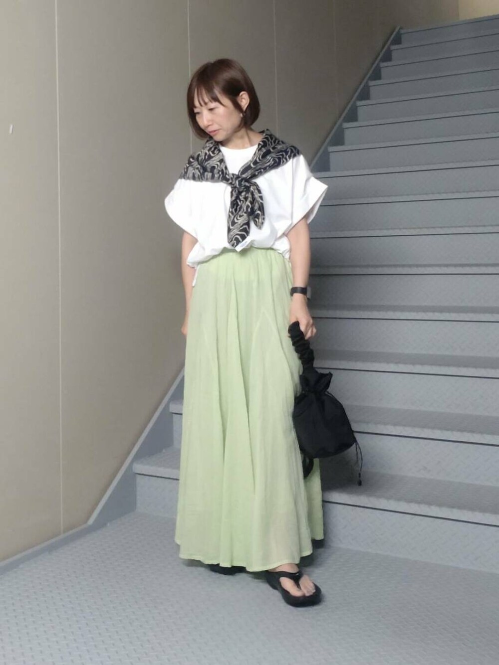 ブラック系のショルダーバッグ、ブラック系のサンダル、グリーン系のスカートを着用したレディースの夏コーディネートの2枚目の写真