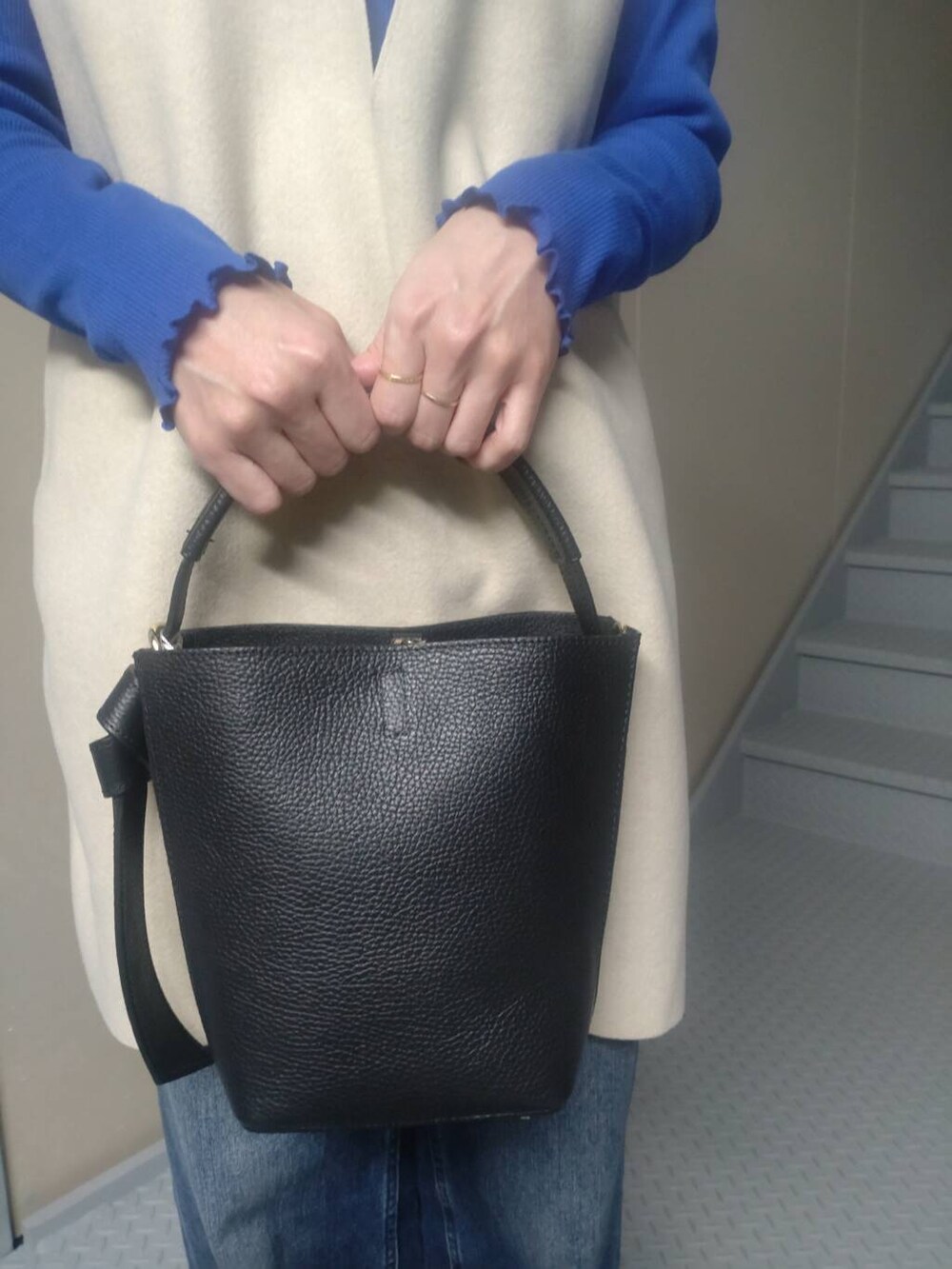 ブルー系のデニムパンツ、ブラック系のショルダーバッグ、ベージュ系のベストを着用したレディースの冬コーディネートの3枚目の写真