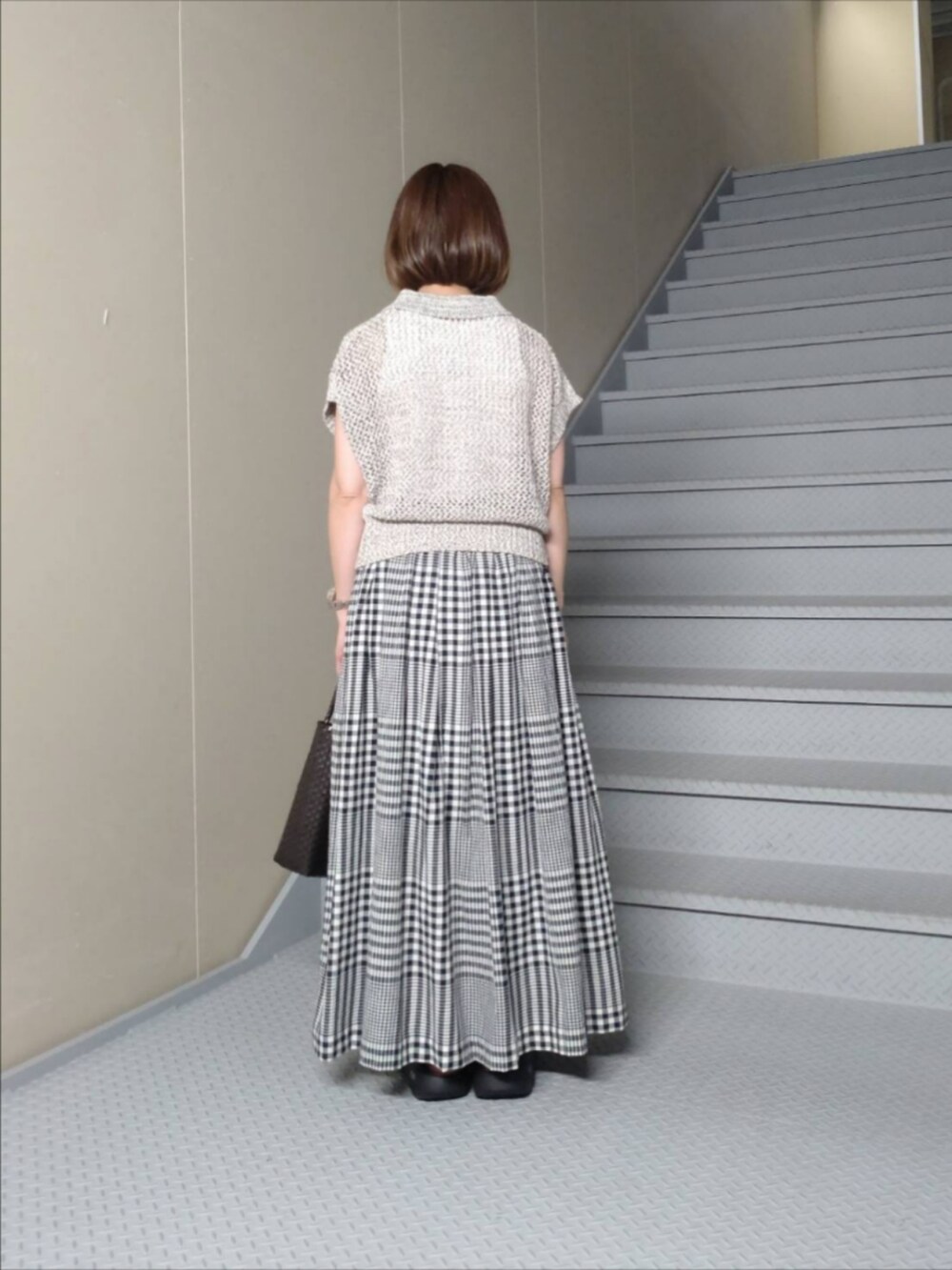 グレー系のニット/セーター、ブラック系のスカート、ブラウン系のトートバッグを着用したレディースの夏コーディネートの2枚目の写真