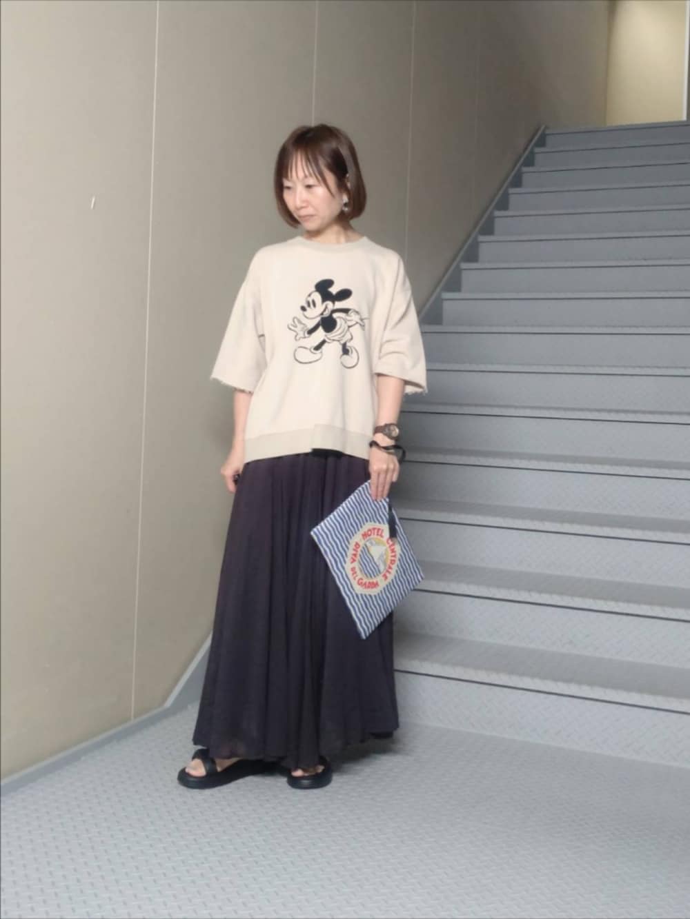 ベージュ系のTシャツ/カットソー、ブラック系のスカート、ブルー系のポーチを着用したレディースの夏コーディネートの2枚目の写真