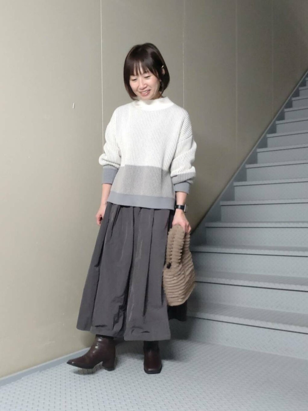 ブラウン系のブーツ、イエロー系のトートバッグ、グレー系のスカートを着用したレディースの冬コーディネートの2枚目の写真