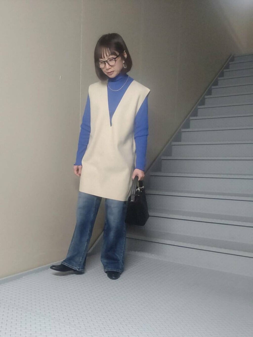 ブルー系のデニムパンツ、ブラック系のショルダーバッグ、ベージュ系のベストを着用したレディースの冬コーディネートの2枚目の写真