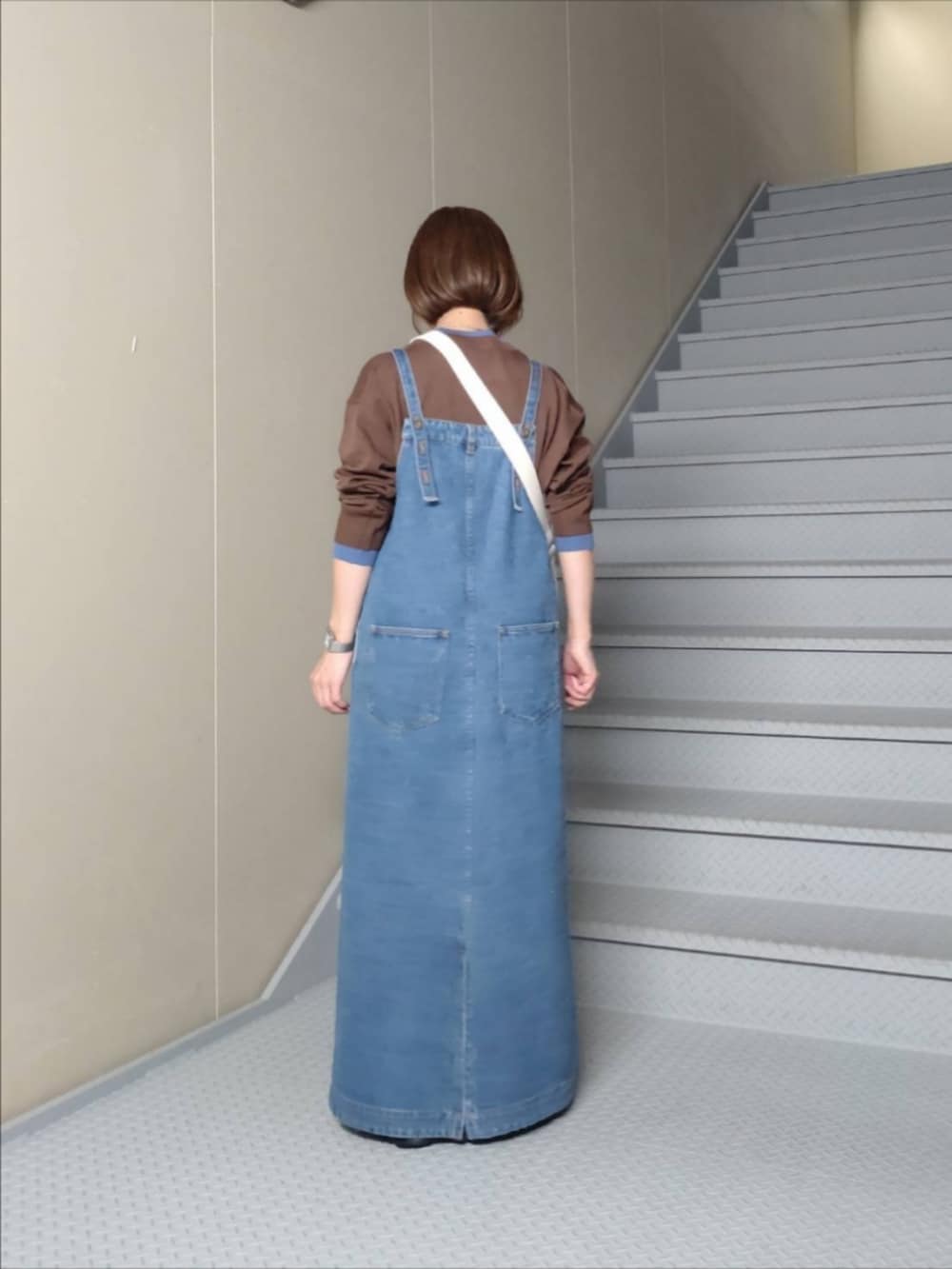 ブルー系のジャンパースカート、ブラウン系のニット/セーター、ホワイト系のショルダーバッグを着用したレディースの秋コーディネートの2枚目の写真