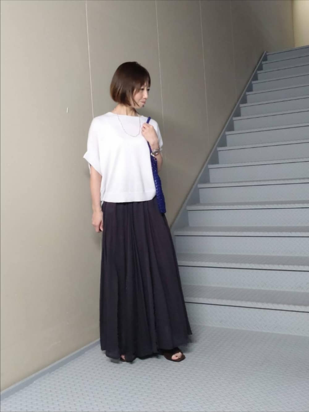 ブラック系のスカート、グレー系のニット/セーター、ブルー系のトートバッグを着用したレディースの夏コーディネートの2枚目の写真