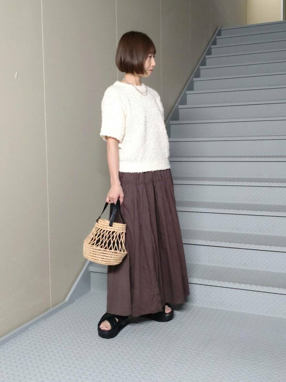 ブラウン系のスカート、ホワイト系のニット/セーター、ブラック系のかごバッグを着用したレディースの春コーディネートの2枚目の写真