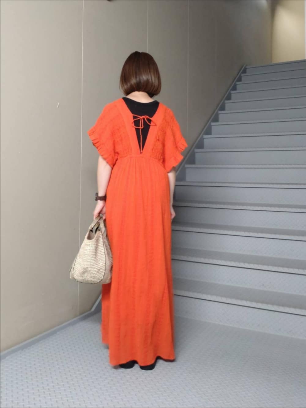 レッド系のワンピース、ベージュ系のハンドバッグ、ブラック系のタンクトップを着用したレディースの夏コーディネートの2枚目の写真