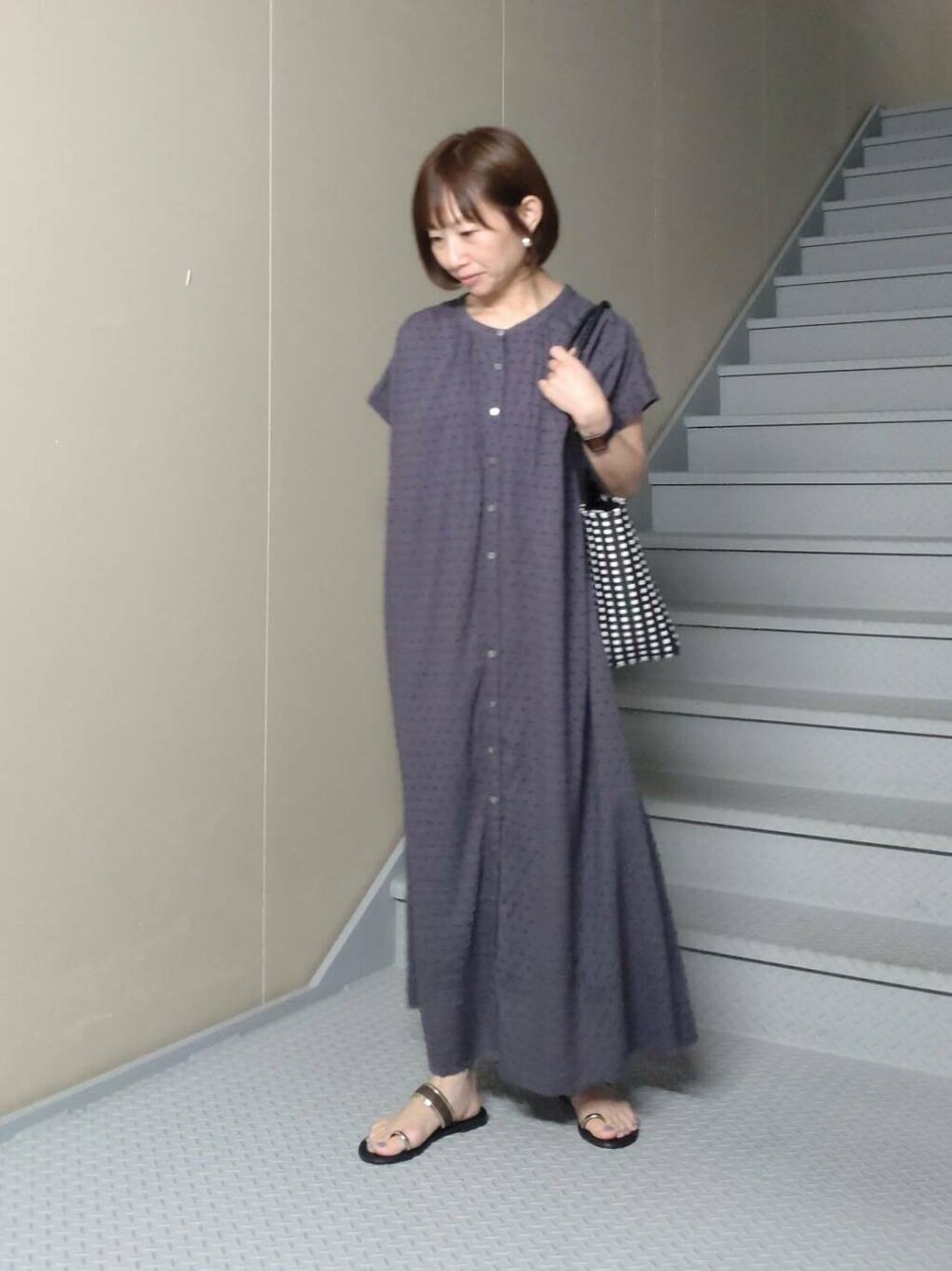 ブラック系のトートバッグ、グレー系のワンピース、ゴールド系のサンダルを着用したレディースの夏コーディネートの2枚目の写真