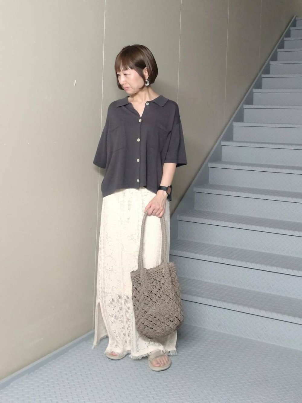 グレー系のトートバッグ、グレー系のニット/セーター、ホワイト系のスカートを着用したレディースの夏コーディネートの2枚目の写真
