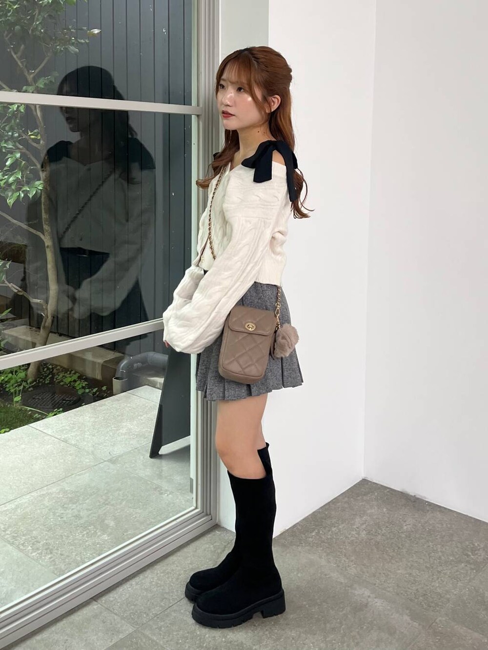 ブラック系のブーツ、グレー系のスカート、ベージュ系のショルダーバッグを着用したレディースの秋コーディネートの2枚目の写真