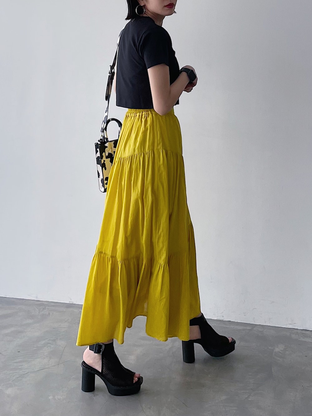 ブラック系のTシャツ/カットソー、イエロー系のスカート、ブラック系のサンダルを着用したレディースの春コーディネートの4枚目の写真