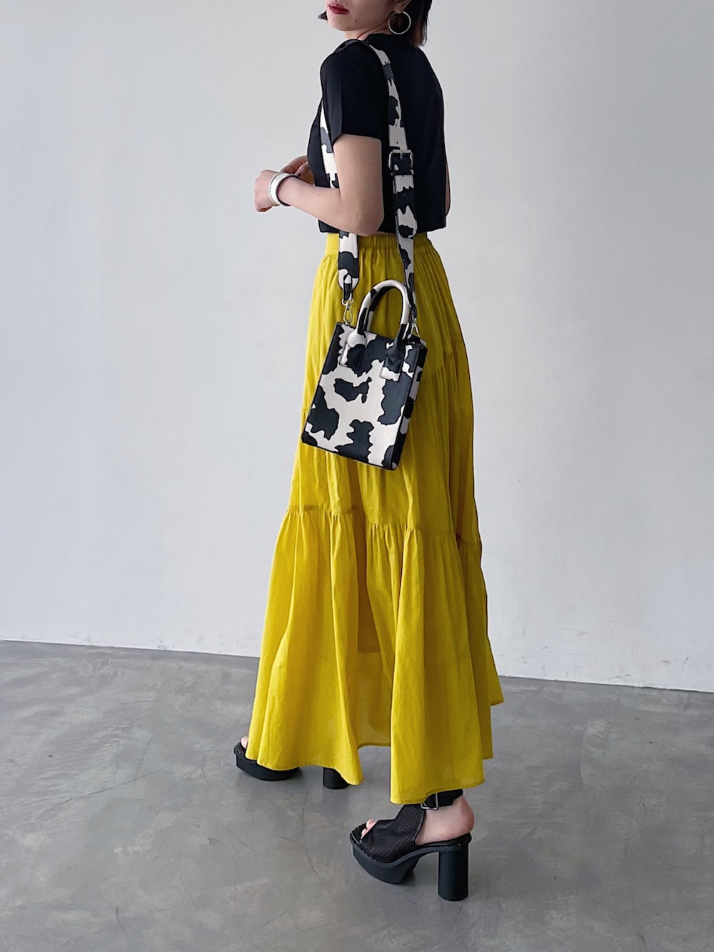 ブラック系のTシャツ/カットソー、イエロー系のスカート、ブラック系のサンダルを着用したレディースの春コーディネートの2枚目の写真