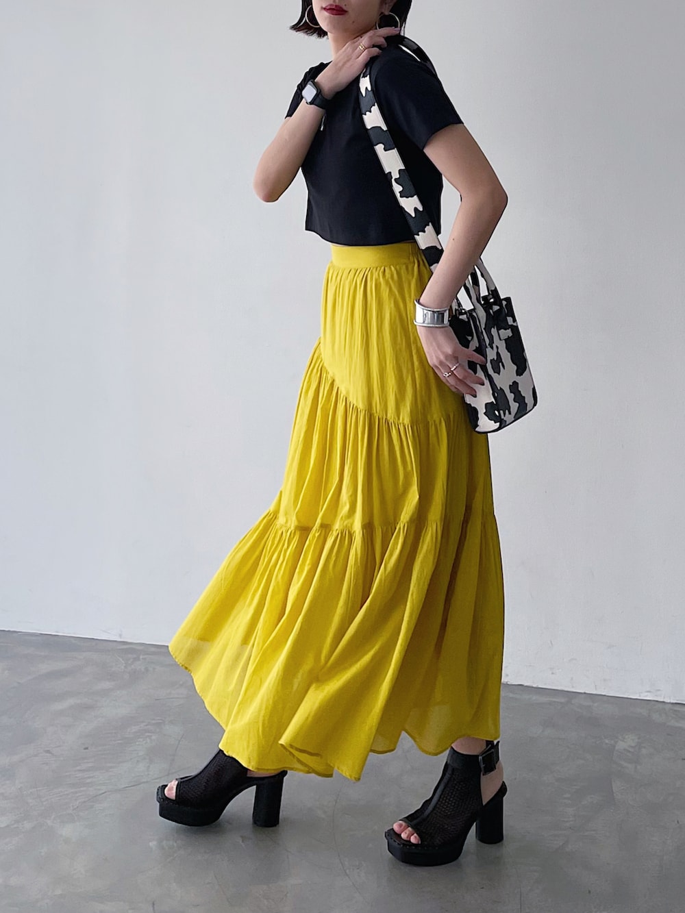 ブラック系のTシャツ/カットソー、イエロー系のスカート、ブラック系のサンダルを着用したレディースの春コーディネートの3枚目の写真