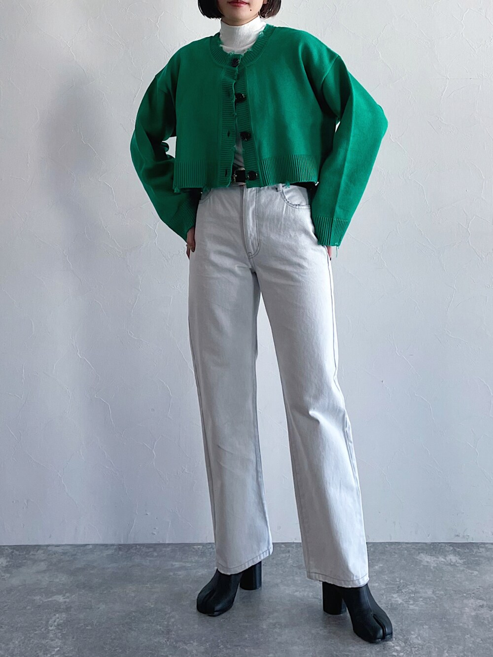 ホワイト系のデニムパンツ、グリーン系のカーディガン/ボレロ、ブラック系のブーツを着用したレディースの冬コーディネートの2枚目の写真