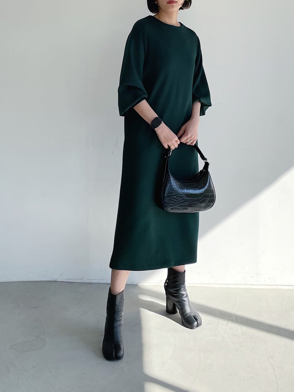 グリーン系のワンピース、ブラック系のブーツ、ブラック系のショルダーバッグを着用したレディースの冬コーディネートの3枚目の写真