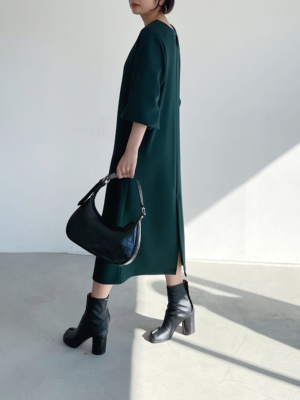 グリーン系のワンピース、ブラック系のブーツ、ブラック系のショルダーバッグを着用したレディースの冬コーディネートの2枚目の写真