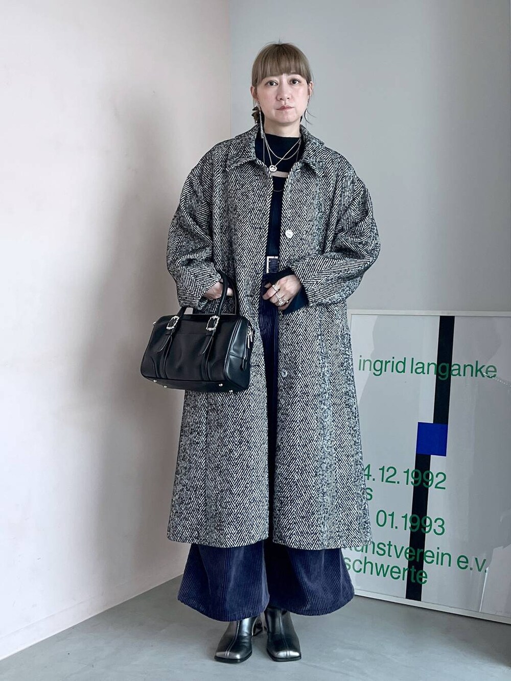 グレー系のステンカラーコート、ブラック系のボストンバッグ、シルバー系のブーツを着用したレディースの秋コーディネートの2枚目の写真