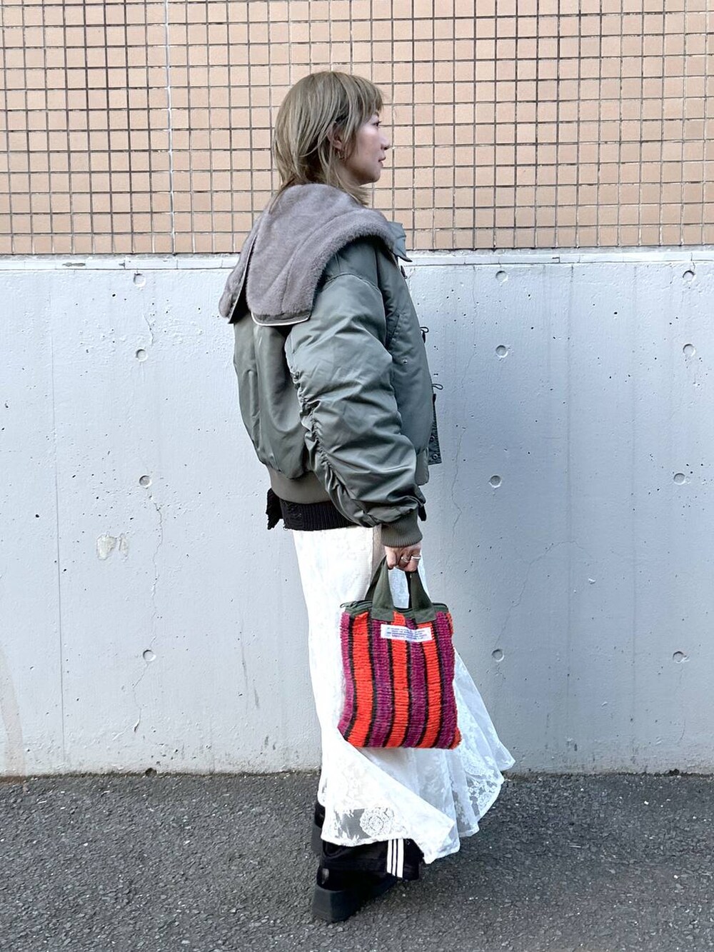 グリーン系のブルゾン、ブラック系のブーツ、ホワイト系のワンピースを着用したレディースの冬コーディネートの5枚目の写真