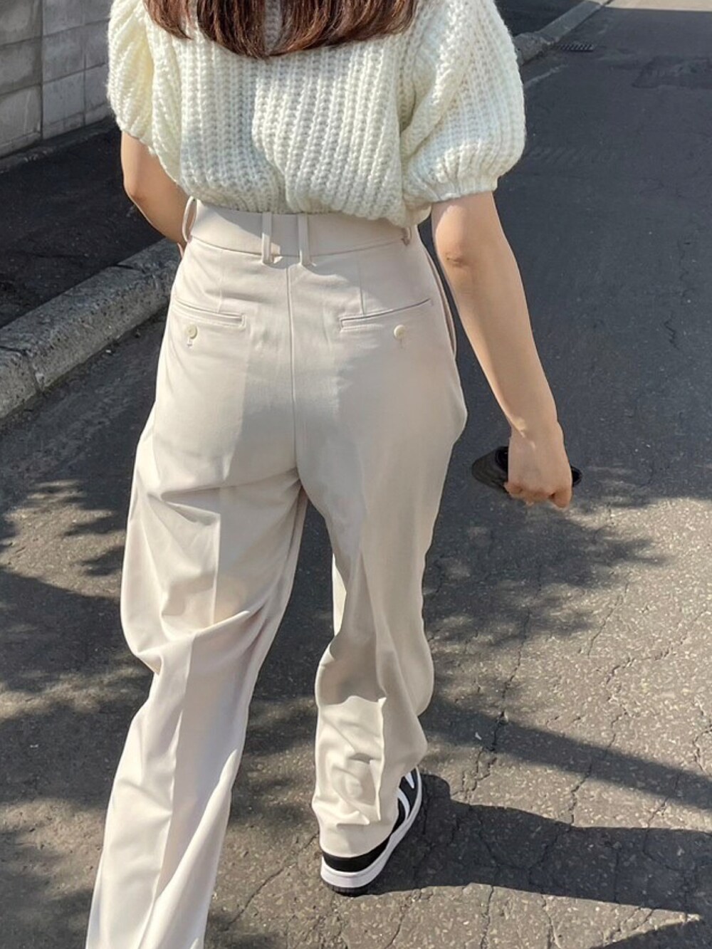 ホワイト系のスラックス、ブラック系のスニーカー、ホワイト系のニット/セーターを着用したレディースの夏コーディネートの3枚目の写真