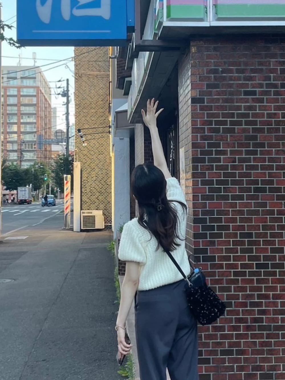 グレー系のスラックス、ブラック系のハンドバッグ、ホワイト系のニット/セーターを着用したレディースの夏コーディネートの2枚目の写真