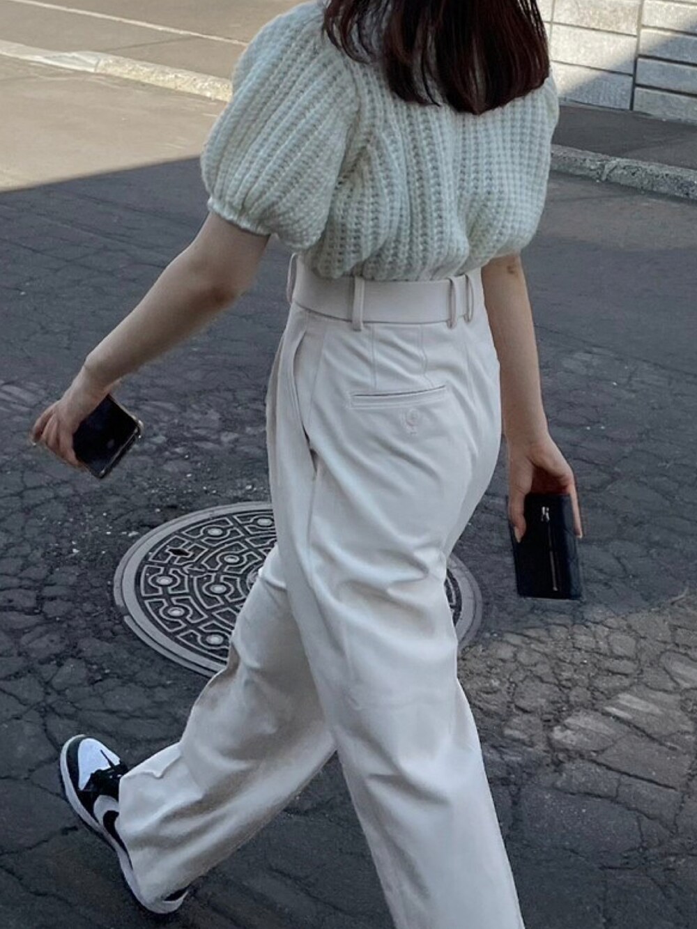 ホワイト系のスラックス、ブラック系のスニーカー、ホワイト系のニット/セーターを着用したレディースの夏コーディネートの2枚目の写真