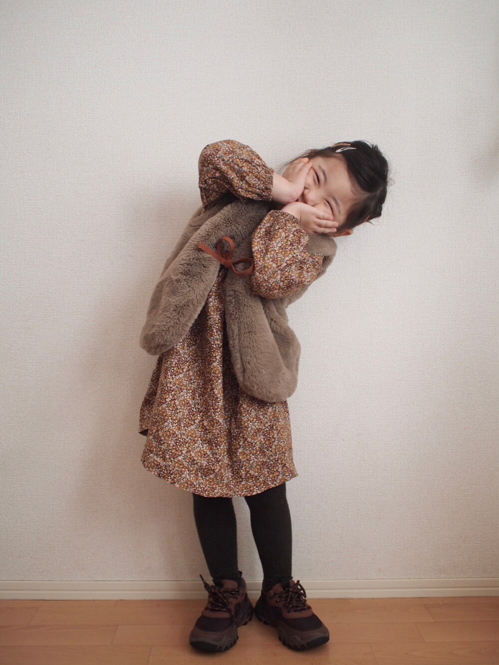 ブラウン系のワンピース、ベージュ系のベスト、ブラウン系のスニーカーを着用したキッズの冬コーディネートの2枚目の写真