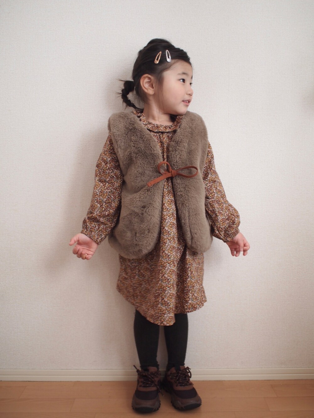 ブラウン系のワンピース、ベージュ系のベスト、ブラウン系のスニーカーを着用したキッズの冬コーディネートの3枚目の写真