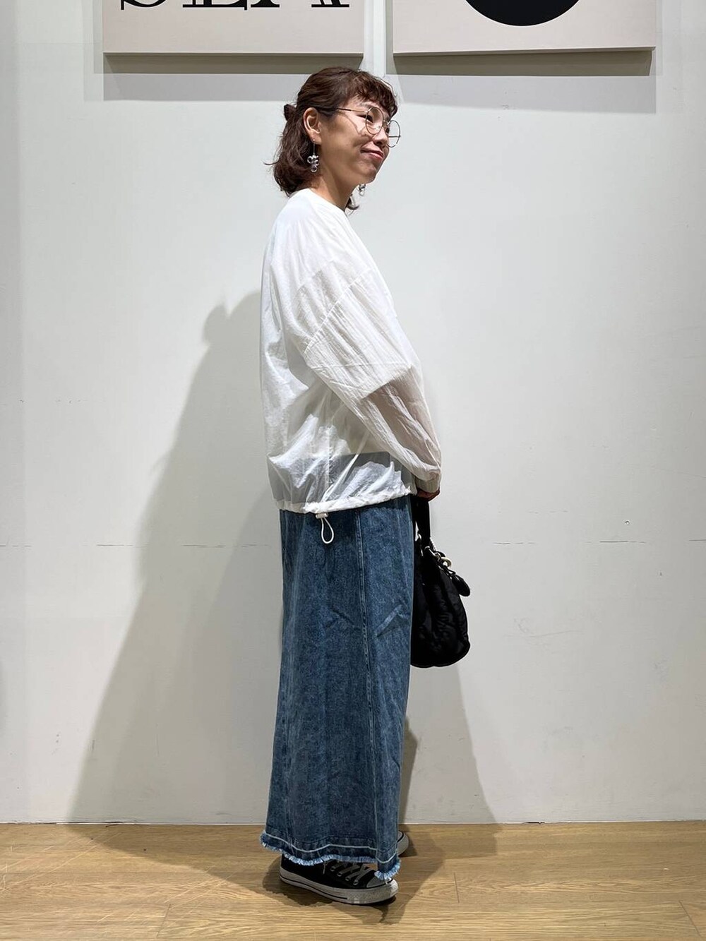 ブラック系のトートバッグ、ブルー系のジャンパースカート、ホワイト系のブルゾンを着用したレディースの夏コーディネートの4枚目の写真
