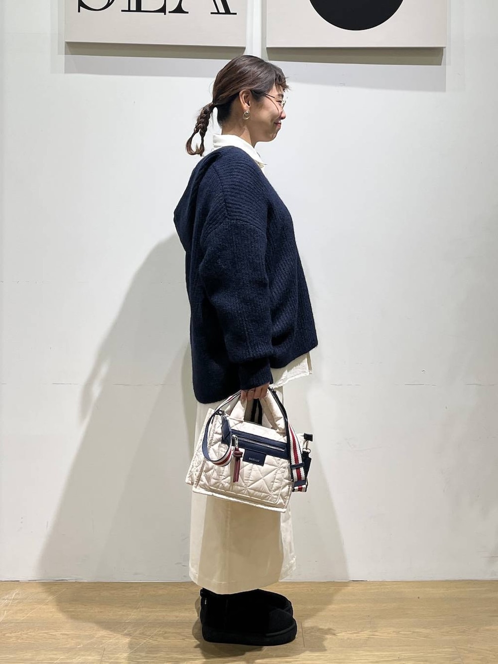 ホワイト系のショルダーバッグ、ベージュ系のスカート、ブラック系のブーツを着用したレディースの秋コーディネートの4枚目の写真