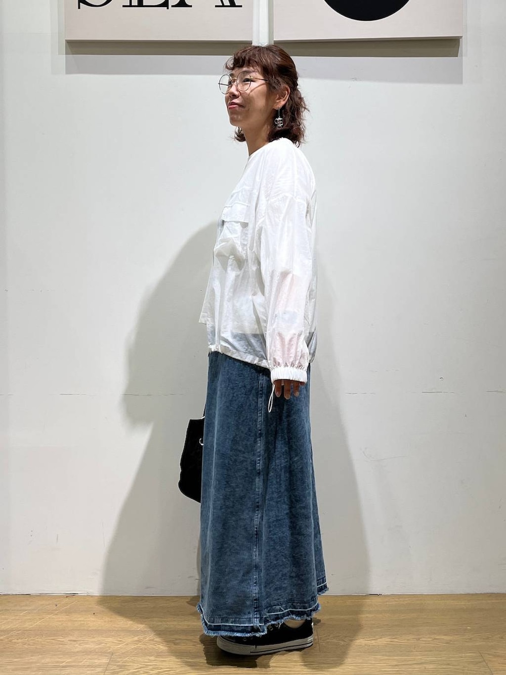 ブラック系のトートバッグ、ブルー系のジャンパースカート、ホワイト系のブルゾンを着用したレディースの夏コーディネートの2枚目の写真