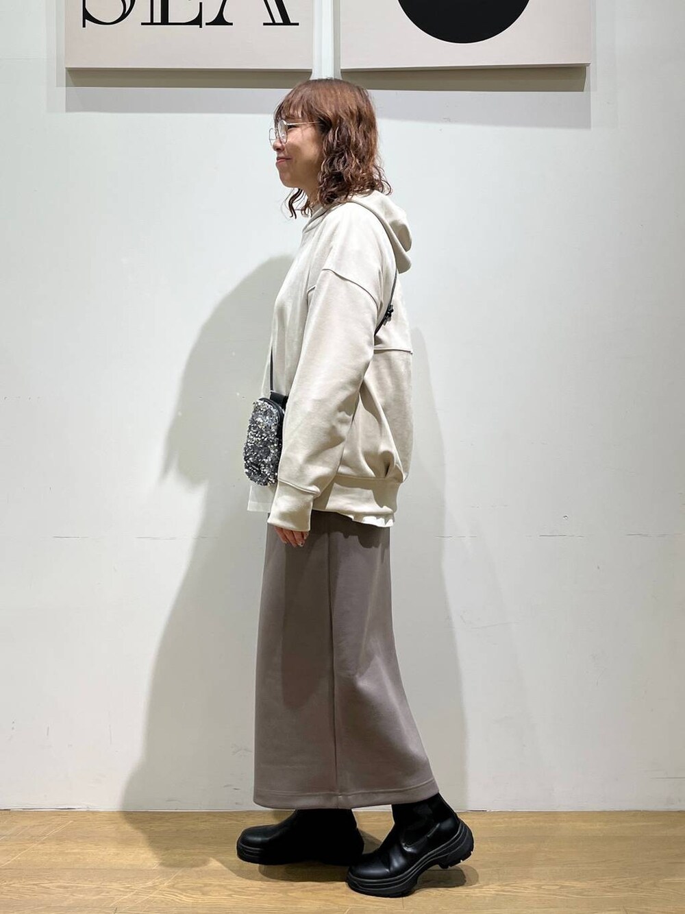 グレー系のショルダーバッグ、ホワイト系のTシャツ/カットソー、ブラック系のブーツを着用したレディースの冬コーディネートの2枚目の写真