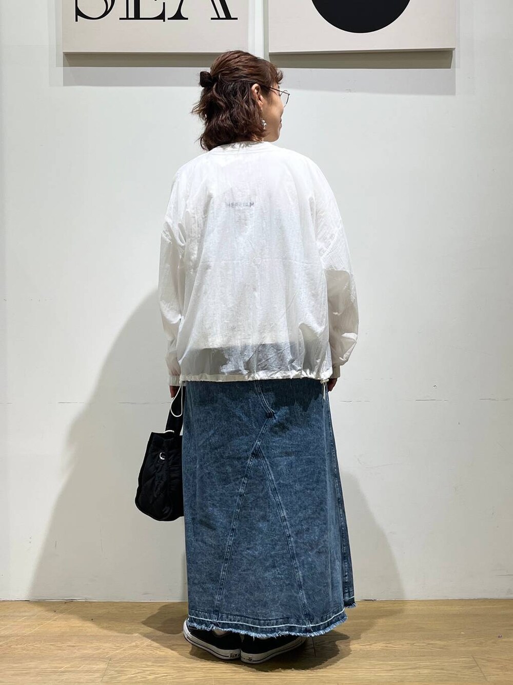ブラック系のトートバッグ、ブルー系のジャンパースカート、ホワイト系のブルゾンを着用したレディースの夏コーディネートの3枚目の写真