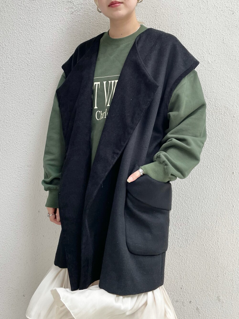 ブラック系のベスト、グリーン系のTシャツ/カットソー、ホワイト系のスカートを着用したレディースの秋コーディネートの3枚目の写真